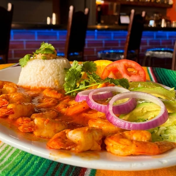 Shrimp dish with rice, avocado, red onion, and tomato on a colorful striped tablecloth.