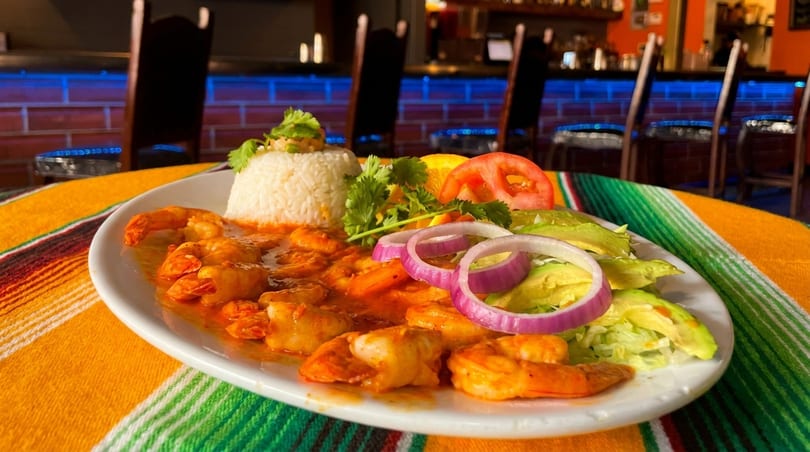Shrimp dish with rice, avocado, red onion, and tomato on a colorful striped tablecloth.