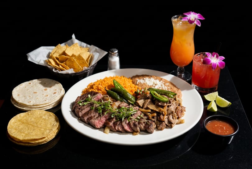 Mexican steak dinner with rice, beans, tortillas, chips, salsa, and two cocktails.