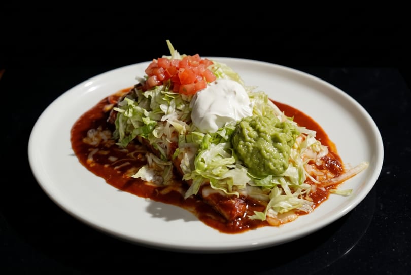 A large burrito covered in red sauce, lettuce, diced tomatoes, sour cream, and guacamole.