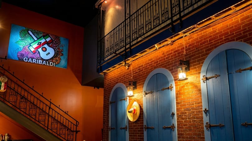Interior of Garibaldi restaurant with a colorful guitar sign, brick wall, blue arched doors, and a balcony.